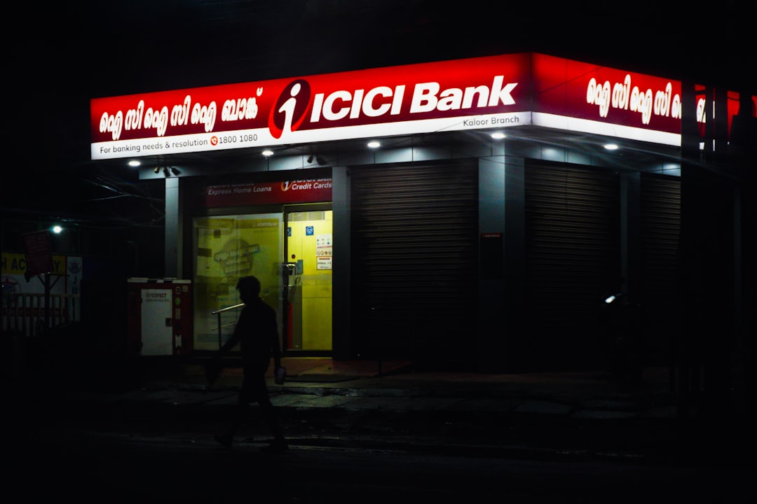 Icici bank building illuminated at night, person walking nearby.